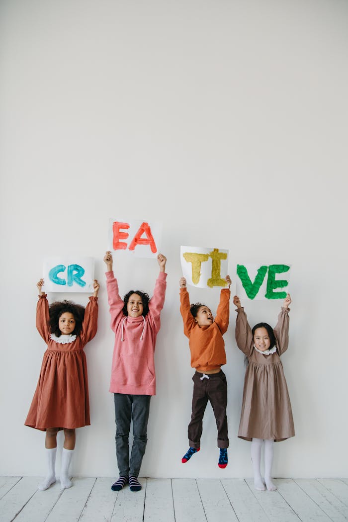 about-02 Group of children holding up colorful letters spelling 'CREATIVE' indoors.